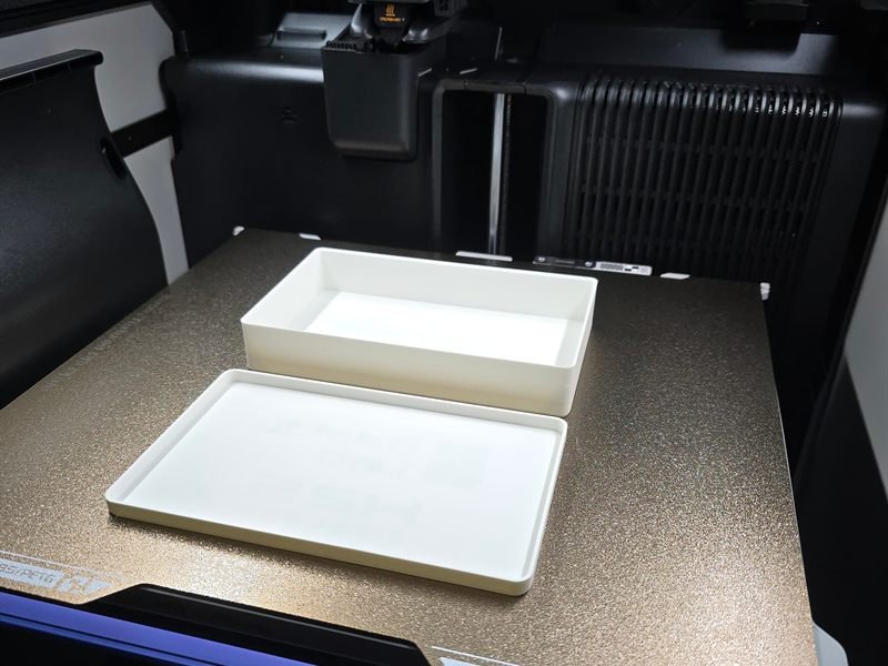 Caja organizadora con tapa impresa en 3D sobre la base de una impresora Bambu Lab